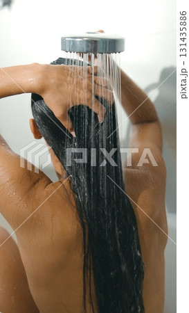 A woman is showering with her long hair flowing beautifully under a soothing waterfall shower 131435886