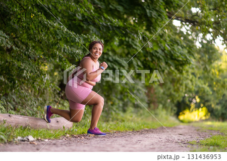Young african american woman doing lunges in the forest and looking determined Young african american woman doing lunges in the forest and looking determined 131436953