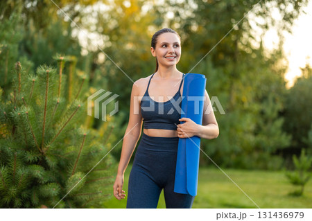 Smiling pretty young woman with a yoga mat looking contented Smiling pretty young woman with a yoga mat looking contented 131436979
