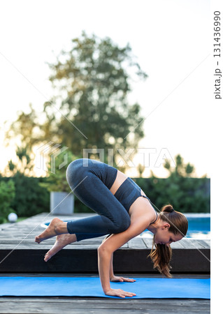 Young long-haired woman standing in bakasana on a yoga mat Young long-haired woman standing in bakasana on a yoga mat 131436990
