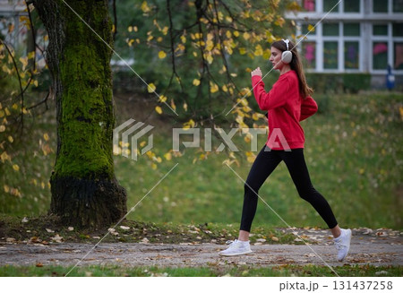 Young beautiful woman running in autumn park and listening to music with headphones on smartphone Young beautiful woman running in autumn park and listening to music with headphones on smartphone 131437258