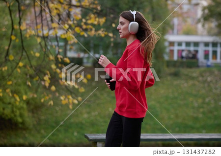 Young beautiful woman running in autumn park and listening to music with headphones on smartphone 131437282
