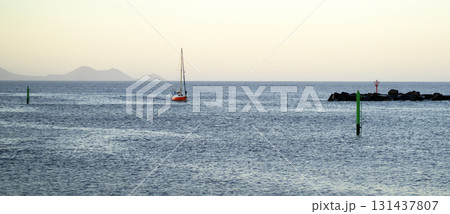 A red yacht sails across the Atlantic Ocean at sunset. A red yacht sails across the Atlantic Ocean at sunset. 131437807
