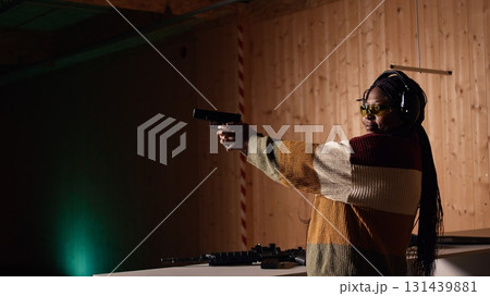 Person wearing safety equipment loading bullets cartridge in pistol during firearm practice session at shooting range. Woman reloading gun, pointing weapon at targets, learning self defense, camera A 131439881