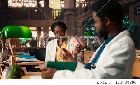 African American dentistry students examining teeth for upcoming exams, learning session on caries prevention using a jaw model in a library. Dedication to oral health education. Camera A. African American dentistry students examining teeth for upcoming exams, learning session on caries prevention using a jaw model in a library. Dedication to oral health education. Camera A. 131439896