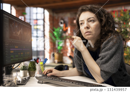 Video creator woman editing a music video on dual monitors in agency studio, multitasking between timeline editing and color grading. Professional editor uses tech tools and software. 131439957