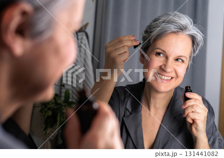 An adult beautiful woman of age during menopause with gray hair applies serum against wrinkles An adult beautiful woman of age during menopause with gray hair applies serum against wrinkles 131441082