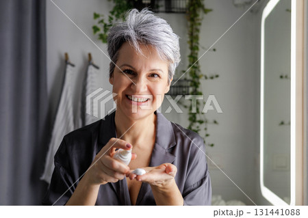 Mature beautiful woman during menopause with gray hair applies hormonal anti-aging cream Mature beautiful woman during menopause with gray hair applies hormonal anti-aging cream 131441088
