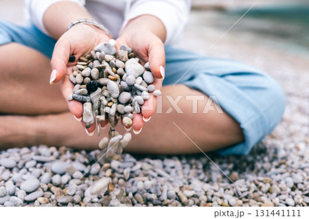 Woman Sitting on Beach Letting Pebbles Fall from Hands Peaceful and Mindful Nature Moment 131441111