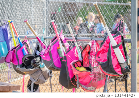 Brightly colored softball bags hang on a chain link fence at a sports field during a practice session in the afternoon sunlight Brightly colored softball bags hang on a chain link fence at a sports field during a practice session in the afternoon sunlight 131441427