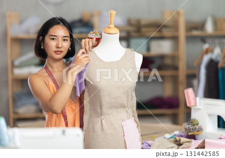 Female tailor sews new dress on a mannequin in sewing studio Female tailor sews new dress on a mannequin in sewing studio 131442585