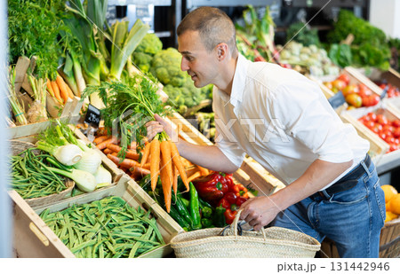 In vegetable department of bio supermarket, male customer took bunch of carrots from window 131442946