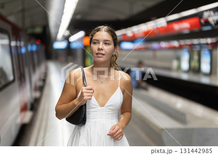 Calm young girl standing on platform of subway station Calm young girl standing on platform of subway station 131442985