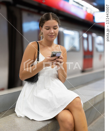 Young woman is sitting on a bench on a platform near a car with a mobile phone Young woman is sitting on a bench on a platform near a car with a mobile phone 131443007