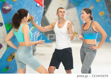 Athletic man and two sporty women discussing climbing options near climbing wall Athletic man and two sporty women discussing climbing options near climbing wall 131443070