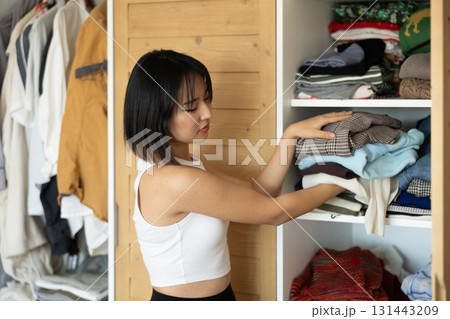 Happy young Asian girl putting some items of clothing in the wardrobe 131443209