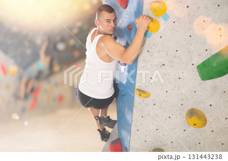 Atlete man grabbing ledges of artificial climbing wall in bouldering centre Atlete man grabbing ledges of artificial climbing wall in bouldering centre 131443238