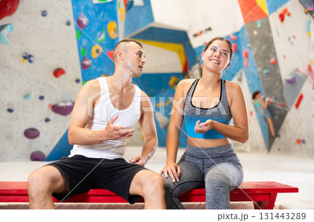 Joyful girl and man share their impressions of climbing climbing wall while sitting on bench in recreation area Joyful girl and man share their impressions of climbing climbing wall while sitting on bench in recreation area 131443289