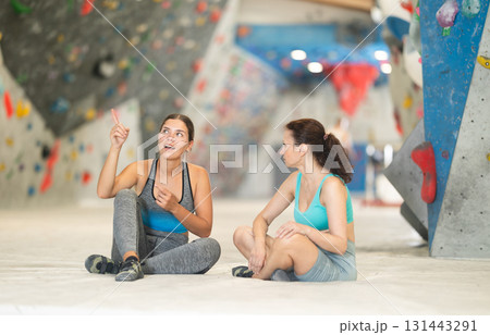 Two athletic women sit on floor and discuss options for climbing a climbing wall without special equipment 131443291