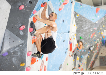 Young man climbing on artificial rock wall in rock-climbing gym 131443293