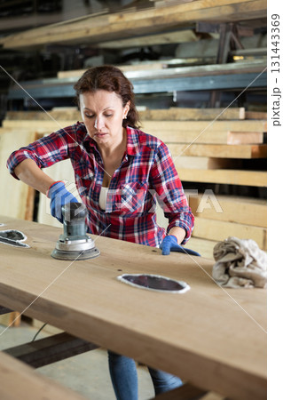 Adult woman polishing oak plank in workshop 131443369