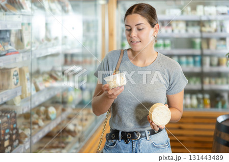 Girl in bio food store holds cheese of different varieties in hands and is thinking about buying Girl in bio food store holds cheese of different varieties in hands and is thinking about buying 131443489