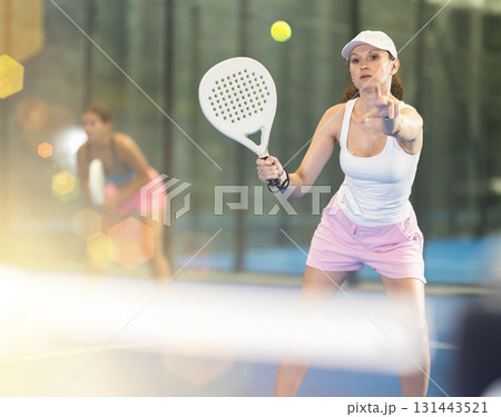 Woman with racket training on outdoor court playing padel game and hitting ball 131443521