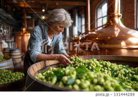 Elderly woman carefully selecting hops in a brewing facility during daytime 131444289