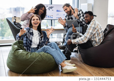 Group of diverse young adults sitting on beanbags in bright modern office posing for selfie. Relaxed and cheerful atmosphere. Ideal for concepts of teamwork, friendship, and modern workplace dynamics. Group of diverse young adults sitting on beanbags in bright modern office posing for selfie. Relaxed and cheerful atmosphere. Ideal for concepts of teamwork, friendship, and modern workplace dynamics. 131444753