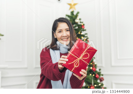 Woman surprise got present gift box on christmas eve. Asian woman holding christmas gift box under xmas tree with smiling face. Woman hands wrap present gift. Merry christmas happy new year concept 131444900