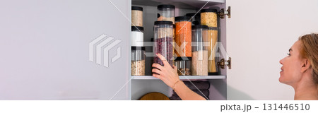 Organized kitchen pantry with cylindrical plastic jar for storing loose products, in grey tones. banner Organized kitchen pantry with cylindrical plastic jar for storing loose products, in grey tones. banner 131446510