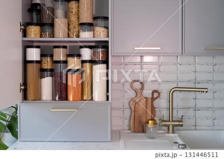 Organized kitchen pantry with cylindrical plastic jar for storing loose products, in grey tones Organized kitchen pantry with cylindrical plastic jar for storing loose products, in grey tones 131446511