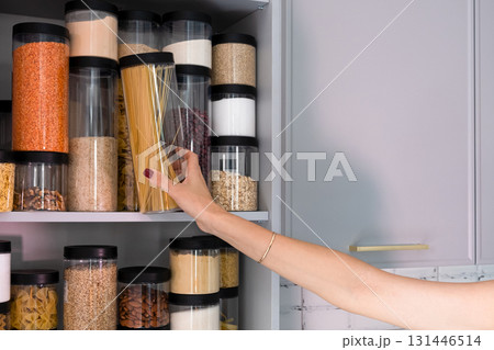 Organized kitchen pantry with cylindrical plastic jar for storing loose products, in grey tones 131446514