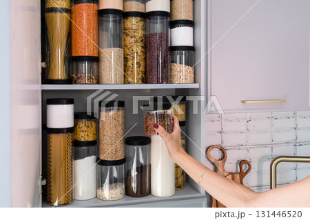 Organized kitchen pantry with cylindrical plastic jar for storing loose products, in grey tones 131446520