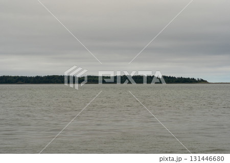 Forested island stretches across calm wide water surface Forested island stretches across calm wide water surface 131446680
