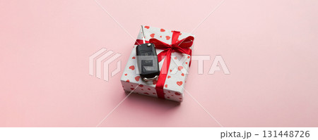 Give gift car key concept top view. Present box with red ribbon bow, heart and car key on coral colored background Give gift car key concept top view. Present box with red ribbon bow, heart and car key on coral colored background 131448726