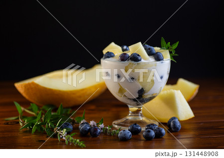 Delicate yogurt with juicy pieces of melon and fresh blueberries on a wooden Delicate yogurt with juicy pieces of melon and fresh blueberries on a wooden 131448908