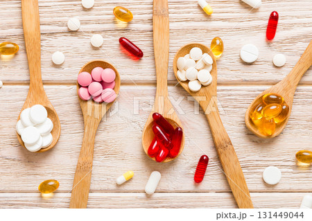Vitamin capsules in a spoon on a colored background. Pills served as a healthy meal. Red soft gel vitamin supplement capsules on spoon 131449044