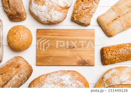 Minimalist wooden cutting board blank mockup on background of Types of homemade bread. Different kinds of fresh bread as background, top view with space for your text or design 131449126
