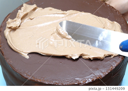 Confectioner woman is smearing cream on sides of cake using spatula, closeup view. culinary, baking and cooking food concept, home cooking 131449209