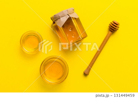 Glass jar of honey with wooden drizzler on colored background. Honey pot and dipper high above. Top view copy space 131449459