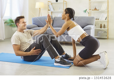 Supportive woman holding feet as man doing sport exercise, sharing a high-five 131451628