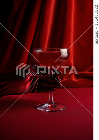 Elegant hand holding cocktail glass against a deep red backdrop, sophisticated cocktail hour concept  131451922