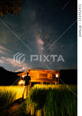 A hut in the middle of a rice field and the belly of a milky way, stars and a night sky with clouds 131452431