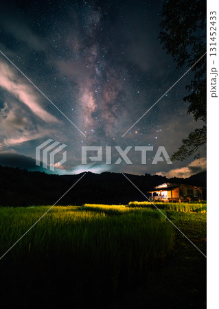 A hut in the middle of a rice field and the belly of a milky way, stars and a night sky with clouds 131452433