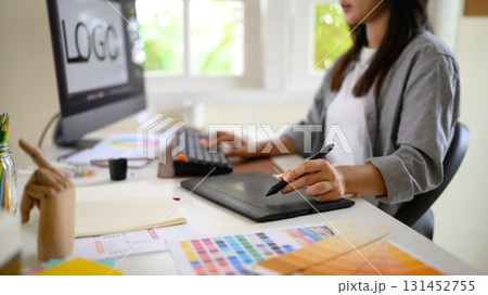 Female graphic designer working at a modern desk using a digital drawing tablet and computer Female graphic designer working at a modern desk using a digital drawing tablet and computer 131452755