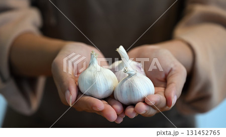 Woman holding three whole garlic bulbs, symbolizing freshness, nutrition, and farm to table lifestyle Woman holding three whole garlic bulbs, symbolizing freshness, nutrition, and farm to table lifestyle 131452765