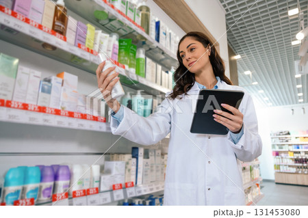 Woman pharmacist reviewing shelves with clipboard in hand Woman pharmacist reviewing shelves with clipboard in hand 131453080