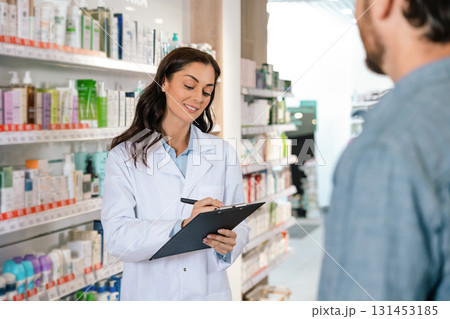Brunette woman pharmacist making notes while consulting client Brunette woman pharmacist making notes while consulting client 131453185