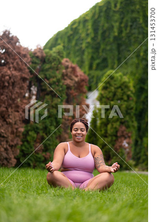 Woman in pink sportswear sitting on a grass on lotus pose and feeling good Woman in pink sportswear sitting on a grass on lotus pose and feeling good 131453700